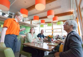 Serveerster neemt bestelling op van een groep gasten in een moderne eetruimte in een vakantiepark met glamping.