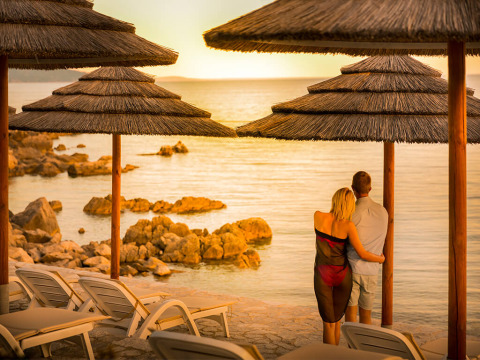 Pareja disfruta de la puesta de sol junto al mar bajo sombrillas cerca de Krk, Primorje-Gorski Kotar, Croacia.