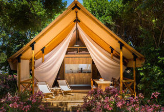 Ein luxuriöses Safarizelt mit Holzterrasse und Liegestühlen inmitten blühender Pflanzen in Camping Krk, Kroatien.