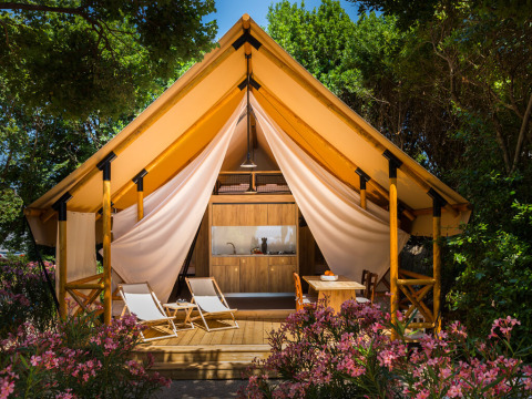 Ein luxuriöses Safarizelt mit Holzterrasse und Liegestühlen inmitten blühender Pflanzen in Camping Krk, Kroatien.