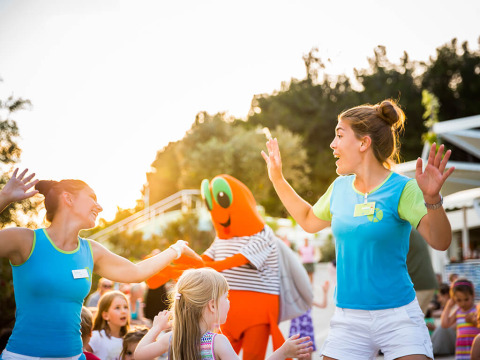 Kinderen en volwassenen dansen en spelen met een oranje mascotte op Valamar Camping Krk in Kroatië.