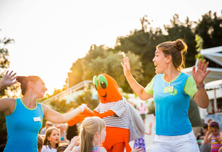 Niños y adultos bailan y juegan felices con una mascota naranja en Valamar Camping Krk en Croacia.