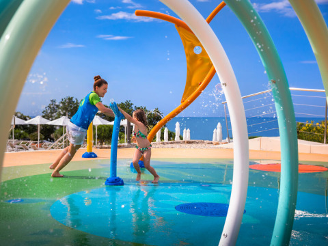 Enfants jouant dans une aire de jeux aquatique colorée à Valamar Camping Krk avec vue sur la mer en Croatie.