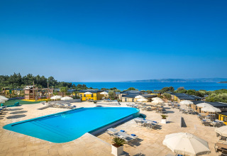 Außenpool eines Lodges mit Liegen, Sonnenschirmen und herrlichem Blick auf das Meer unter blauem Himmel.