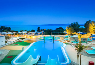 Kinderzwembad met glijbanen en ligstoelen bij Valamar Camping Krk, Kroatië, in de avondschemering.