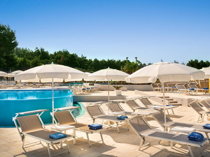 Sonnige Liegestühle und Sonnenschirme am Pool einer ruhigen Lodge, umgeben von Bäumen und blauem Himmel.