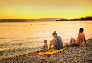 En familie sidder på småsten ved solnedgang ved kysten på Valamar Camping Krk i Kroatien.