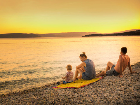 Gezin zit op kiezelstrand bij zonsondergang aan zee op Valamar Camping Krk, Kroatië.