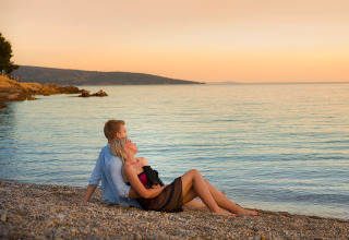 Un couple romantique assis sur une plage de galets près de Krk, Croatie, admire le coucher du soleil.