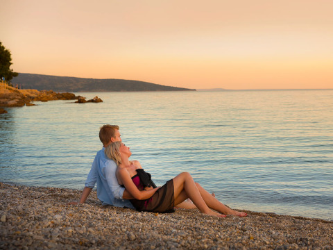 Una coppia romantica seduta su una spiaggia di ciottoli vicino a Krk, Croazia, al tramonto sul mare.