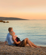 Een romantisch stel op een kiezelstrand nabij Krk, Kroatië, geniet samen van de zonsondergang.