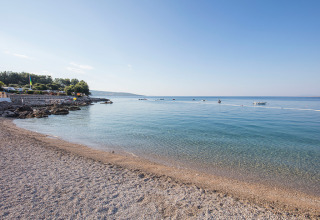Costa nei dintorni di Krk, Croazia, con mare limpido, spiaggia di ciottoli, barche e cielo sereno.