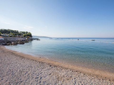 Paysage côtier près de Krk en Croatie, plage de galets, mer calme, petits bateaux et ciel bleu dégagé.