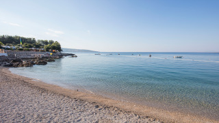 Kust bij Krk, Kroatië met helderblauw water, kiezelstrand, kleine bootjes en een heldere hemel.