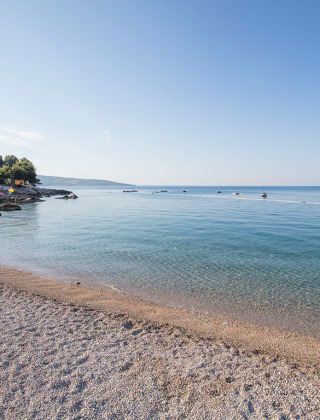 Kust bij Krk, Kroatië met helderblauw water, kiezelstrand, kleine bootjes en een heldere hemel.