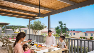 Gezin ontbijt op het terras van Krk Home lodge met zeezicht en vakantiehuisjes op de achtergrond.