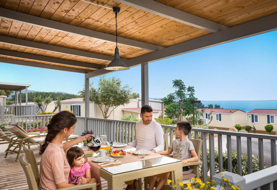 Gezin ontbijt op het terras van Krk Home lodge met zeezicht en vakantiehuisjes op de achtergrond.