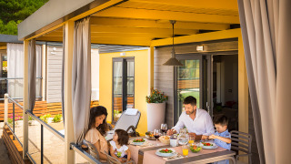 Gezin eet samen op het overdekte terras van Bella Vista Home Lodge, omringd door natuur en licht.