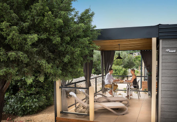 Par nyder et måltid på en afslappende terrasse på Bella Vista Chalet omringet af grønne træer og planter.
