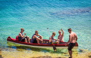 Five men relaxing in a canoe on clear blue water near Premantura, Istria, Croatia, by the rocky shore.