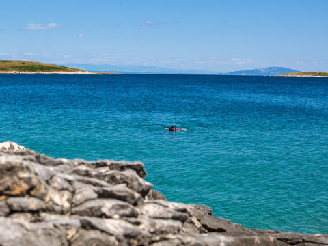 Ein Schnorchler schwimmt im klaren blauen Wasser bei Camping Arena Stupice in Istrien, Kroatien, mit Felsen im Vordergrund.