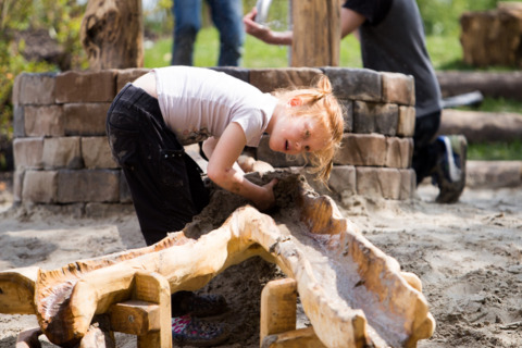 Kind speelt met zand en water bij houten constructie op een glamping vakantiepark in de buitenlucht.