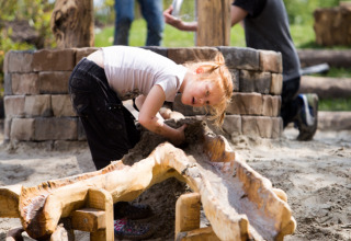 Kind speelt met zand en water bij houten constructie op een glamping vakantiepark in de buitenlucht.
