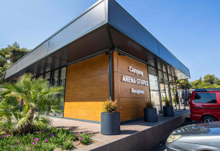 Edificio moderno de recepción en Camping Arena Stupice en Istria, Croacia, con autos y área ajardinada al frente.