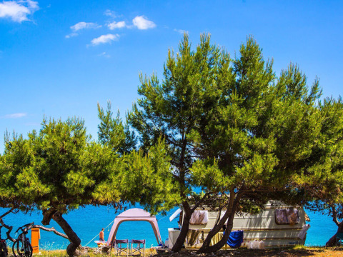 Campeggio Arena Stupice a Istria, Croazia, con roulotte, tenda e vista sul mare tra gli alberi di pino.