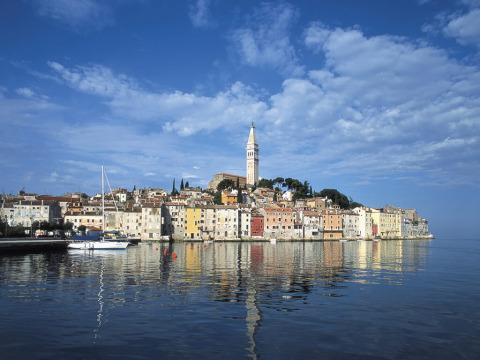 Colorful seaside buildings in Rovinj, Istria, Croatia with a prominent church tower and reflecting water.