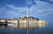 Bunte Häuser am Wasser in Rovinj, Istrien, Kroatien, mit Kirchturm und Segelboot bei klarem Himmel.