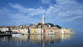 Kleurrijke gevels in Rovinj, Istrië, Kroatië, met kerktoren en reflectie op het kalme water.