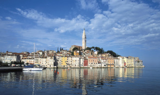 Kleurrijke gevels in Rovinj, Istrië, Kroatië, met kerktoren en reflectie op het kalme water.