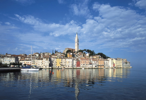 Case colorate sul mare a Rovigno, Istria, Croazia, con un alto campanile e acqua riflettente.