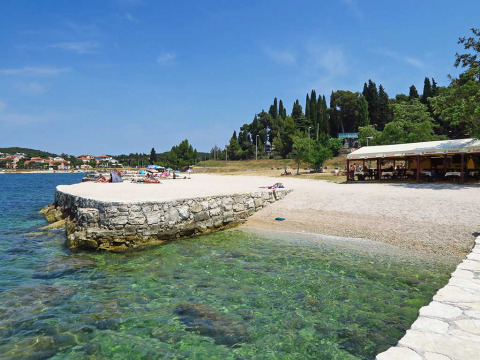 Beach scene with clear water at Camping Porton Nature Hideouts holiday park in Istria, Croatia, with sunbathers.