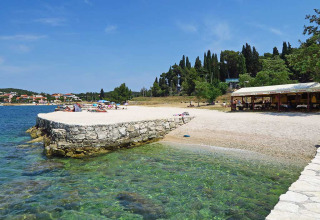 Beach scene with clear water at Camping Porton Nature Hideouts holiday park in Istria, Croatia, with sunbathers.