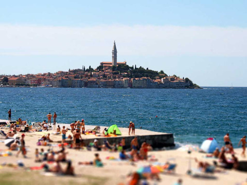 Scena di spiaggia con villeggianti a Camping Porton Nature Hideouts, Istria, Croazia, città e mare sullo sfondo.
