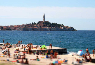 Scena di spiaggia con villeggianti a Camping Porton Nature Hideouts, Istria, Croazia, città e mare sullo sfondo.