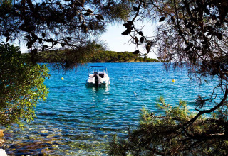 Boot aangemeerd in helderblauw water tussen dennen bij Baia Holiday Poljana in Kroatië.