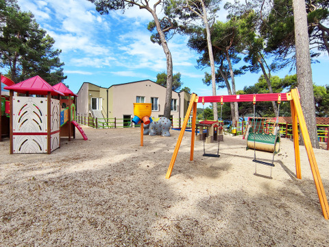 Spielplatz mit Schaukeln, Rutsche und Häuschen im Baia Holiday Poljana Park, Kroatien, an einem sonnigen Tag.