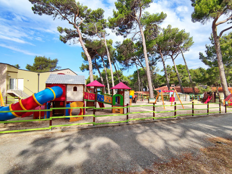 Colorful playground with slides and swings at Baia Holiday Poljana holiday park, surrounded by tall pine trees.