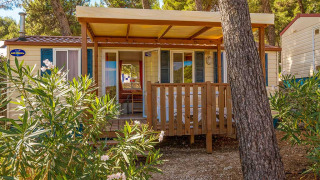 Veranda in legno davanti al lodge Blu Romantic al Baia Holiday Poljana, Croazia, circondata da pini.