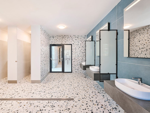 Salle de bain moderne avec sol en terrazzo, grands miroirs, lavabos et douches à l’Aminess Style Camping Avalona Resort.