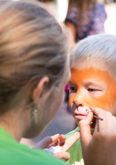 Een jonge jongen krijgt zijn gezicht geschminkt door een vrouw tijdens een kinderactiviteit op een vakantiepark.