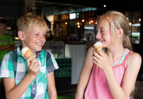 Twee kinderen genieten samen van een ijsje in een gezellige vakantieparksetting met glamping faciliteiten.