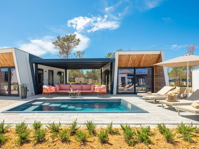Moderne glamping-villa med privat pool, solstole, parasoller og udendørs lounge, omgivet af natur.