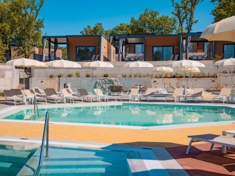 Poolbereich mit Sonnenliegen, weißen Sonnenschirmen und modernen Ferienhäusern im Aminess Style Camping Atea Resort, Kroatien.