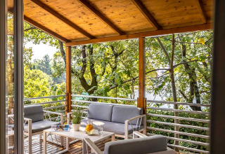 Covered wooden terrace with modern outdoor seating, surrounded by lush trees at Aminess Style Camping Atea Resort.