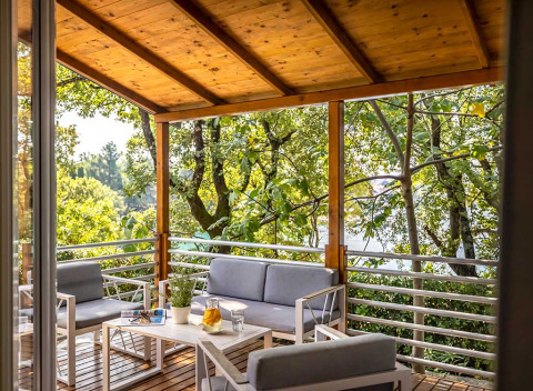 Udendørs terrasse med moderne havemøbler, trætag og udsigt til grønne træer på Aminess Style Camping Atea Resort.