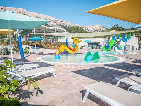 Zona de piscina para niños con tumbonas, juguetes y toboganes acuáticos en Valamar Camping Baška, Croacia.